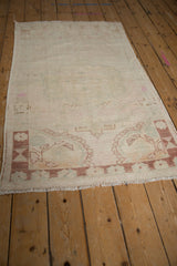 Distressed vintage Oushak rug, showing low pile, faded ivory patterns, and fringe.