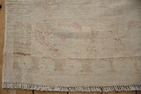 Distressed vintage Oushak rug showing worn texture, ivory and faint pink tones, selvage, and fringe.