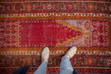 A standing view of the vintage Ghiordes rug's prayer niche and time-softened cherry red field.