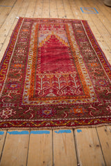 Angled view of a Ghiordes prayer runner, highlighting its full length and warm, time-softened red field.