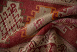 Textured distressed Kurd runner pile showing raspberry red, tangerine, and ivory geometric pattern.