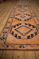 Textured tangerine orange field with distressed navy geometric medallions on a Kurd runner.
