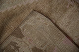 Distressed beige pile, neatly secured edge, and hand-knotted foundation of a vintage Oushak rug.