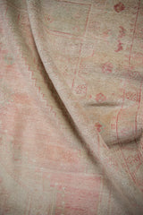 Distressed vintage Oushak rug fold, showing worn pile texture in dusty pink and platinum.