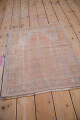 Angled view of a distressed Oushak prayer rug with a faded dusty rose and seafoam green palette.