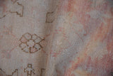 Distressed Oushak rug pile showing worn floral motifs in dusty rose and ivory.