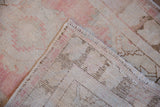 Distressed Oushak rug corner showing worn dusty rose pile, intact side cord selvages, and a hand-knotted foundation.