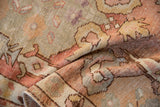 Folded close-up of distressed vintage Oushak rug with low pile and faded sage, orange, rose patterns.