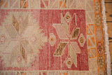 Distressed Kurd runner: raspberry red serrated medallion, starburst floral motif, fringe, and visible knot head wear.