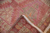 Distressed Kurd rug geometric pattern in dusty red tones, showing knotted back and fringe.