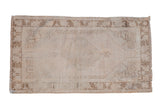 Distressed vintage Oushak rug featuring an ivory field, muted brown diamond medallion, and floral border.