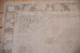 Distressed vintage Oushak rug corner shows worn ivory pile, visible foundation, and faded brown patterns.