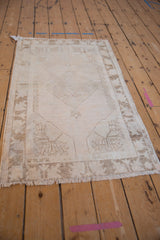 Distressed Oushak rug's ivory diamond medallion, floral spandrels, and even knot wear.
