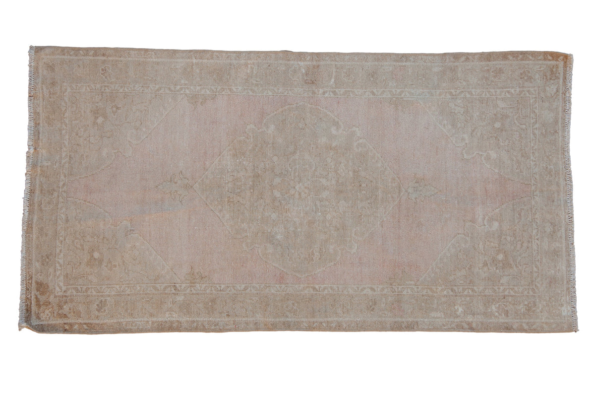 Vintage distressed Oushak runner with a faded medallion on a dusty mauve and beige abrashed field.