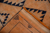Distressed Kurd runner's folded corner, revealing textured tangerine pile, navy primitive motifs, and foundation.