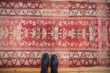 A vintage distressed Kurd runner's decorative starburst pattern in cherry red, dusty rose, and ivory, viewed from overhead.