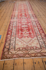 A long, angled view of the vintage Kurd runner, highlighting its distressed red and ivory pattern.