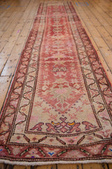 A long vintage Kurd runner with a distressed, abrashed red field and meandering vine border.