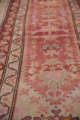 Low angle view along a distressed Kurd runner, showing its meandering vine border and abrashed red field.