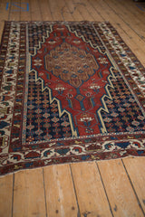 A traditional vintage Hamadan rug shown from an angle, highlighting its red medallion and navy field.