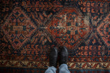 Section of vintage Persian Mehreban rug with blush medallion, worn ruby red field, and intricate cobalt blue motifs.