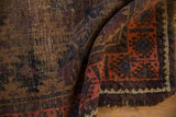 Folded antique Belouch rug edge revealing a blush striated border and aubergine, brown patterns.