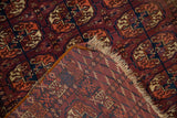 Folded edge of fine Turkmen rug, showing geometric elephant's footprint guls and woven foundation with tattered fringe.