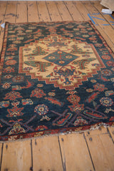 Angled view of a vintage Borchalou rug's stepped medallion and navy field with pictorial motifs.