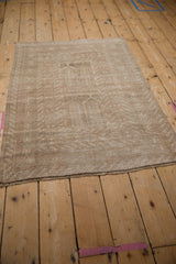 Vintage distressed Turkmen rug from an angle, with a soft beige and sand geometric pattern.