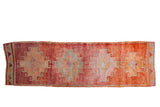 Distressed Kurd vintage rug runner with geometric hook medallions in raspberry red, pale rust, and silver.