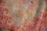 Close-up of the distressed, hand-knotted pile showing abrashed raspberry and orange tones.