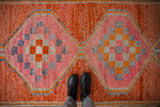 Distressed Kurd runner, pink and orange checkerboard medallions, textured geometric pile, with boots.