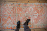 Textured pile of vintage distressed Kurd runner showing tangerine and beige geometric medallions.