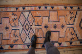 Overhead view showing the worn texture and tangerine orange geometric pattern of a distressed Kurd runner.