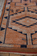 Textured wear across the knot heads of a distressed Kurd runner with tangerine and navy tones.