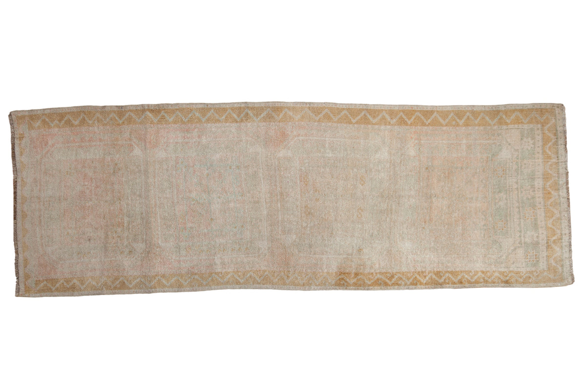 Distressed Oushak rug runner with faded gul medallions in pale pink, seafoam, and dusty gold.