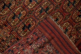 Folded corner of antique Turkmen rug reveals geometric guls, striped foundation, and tattered fringed end.