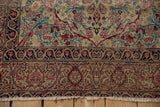 Antique Kerman rug's fringe and lower intricate border with navy blue, dusty gold, and cochineal red floral motifs.