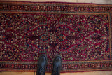 Overhead view of a vintage American Sarouk runner with boots for scale, showing the cherry red floral pattern.
