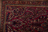Finely detailed floral sprays and navy blue vines on the cherry red pile of a vintage Sarouk rug corner.