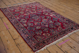 Vintage German Sarouk rug with cherry red field and allover floral sprays shown at an angle.