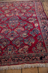 Angled view of a vintage Sarouk rug corner, showing the cherry red field, navy border, and fringe.