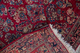 A folded corner reveals the woven foundation and dense floral pile of a fine Sarouk rug.