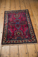 Angled view of a vintage Persian Lilihan rug with a floral raspberry red field and nuanced beige border.