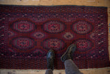 Vintage Turkmen rug with prominent burgundy field, fuchsia guls, navy accents, and visible tattered fringe.