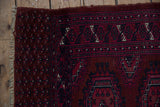 Vintage Turkmen rug corner detail: burgundy field with minor guls, geometric border, tattered fringe.