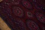 Vintage Turkmen rug detail: prominent burgundy guls, navy border, patinated pile, and frayed edge.
