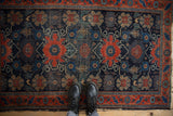 Antique Senneh rug, navy and cherry red floral vinery, visible wear, tattered ends, with feet.