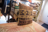 Detail of vintage rug fragment pillow's hand-knotted geometric patchwork in earthy and purplish-red tones.