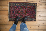 Vintage Persian Borchalou mat showing scale and rich fuchsia floral pattern on a wood floor.